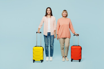 Elder parent mom with young adult daughter two women wear casual clothes hold suitcase bag isolated on plain blue background Tourist travel abroad in free time rest getaway. Air flight trip concept.