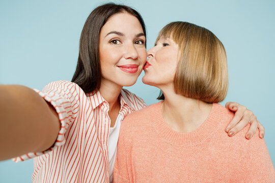 Close up elder parent mom with young adult daughter two women together wear casual clothes do selfie shot pov on mobile cell phone kiss hug isolated on plain blue cyan background. Family day concept.