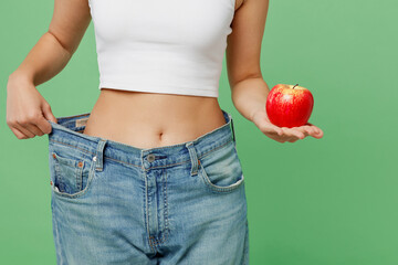 Cropped young woman wears white clothes show loose pants on waist after weightloss hold red apple...