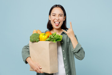 Fototapeta na wymiar Young happy woman wears casual clothes hold brown paper bag with food products show horns up gesture isolated on plain blue cyan background studio portrait. Delivery service from shop or restaurant.