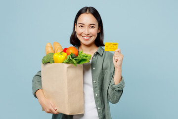 Fototapeta na wymiar Young fun woman in casual clothes hold brown paper bag with food products mock up of credit bank card isolated on plain blue cyan background studio portrait. Delivery service from shop or restaurant