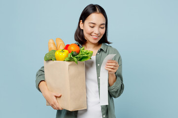 Fototapeta na wymiar Young smiling happy fun woman in casual clothes hold brown paper bag with food products look at check isolated on plain blue cyan background studio portrait. Delivery service from shop or restaurant