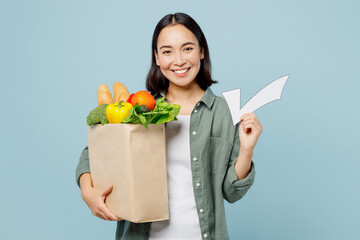 Young smiling happy woman wear casual clothes hold brown paper bag with food products check mark sign isolated on plain blue cyan background studio portrait. Delivery service from shop or restaurant.