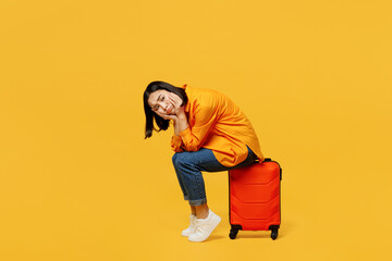 Side view sad young woman wears summer casual clothes sit on suitcase bag isolated on plain yellow...
