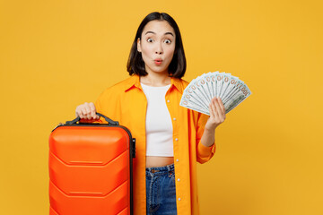 Young woman in summer casual clothes hold in hand fan of cash money dollar isolated on plain yellow background. Tourist travel abroad in free spare time rest getaway. Air flight trip journey concept