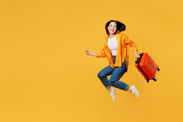 Fototapeta na wymiar Side view fun young woman in summer casual clothes jump high hold suitcase isolated on plain yellow background. Tourist travel abroad in free spare time rest getaway. Air flight trip journey concept