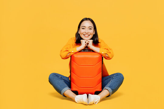 Young smiling woman wear summer casual clothes sit near suitcase look camera isolated on plain yellow background. Tourist travel abroad in free spare time rest getaway Air flight trip journey concept.