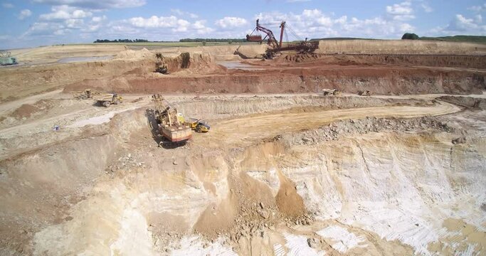 large quarry territory with dump trucks driving against bucket wheel excavator under blue sky with clouds aerial view
