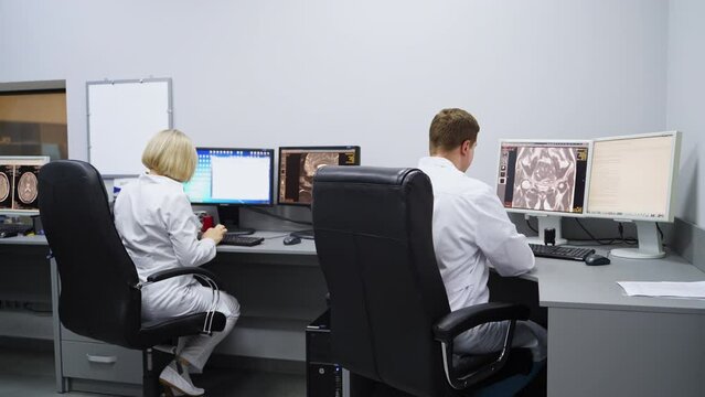 Laboratory room for magnetic resonance imaging analysis. Male and female colleagues sit at computers checking the scans.