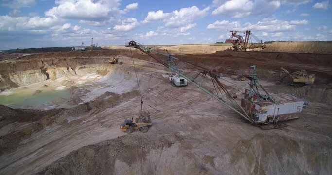 large grey metal crane bagger loads dump truck with overburden ground among quarries under cloudy sky aerial view