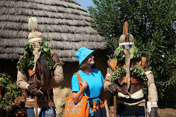 Tourist fashion woman and Bassari men in masks in traditional national costumes in Kedougou, Senegal. Bassari people, African folk mask. Bassari ethnicity. Tribal, native Senegalese people. Tribe