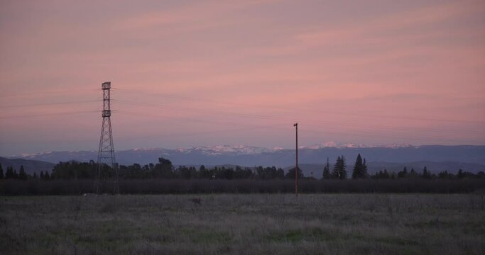 A pastel sky over the Sierra Nevada mountains with power lines and a field in the foreground in Clovis, CA, USA