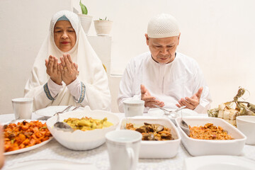 Muslim family are praying together before eat special dish on eid moment, hand raised and bow head. Eid Mubarak ramadan celebration.