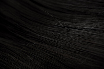 Brunette or black hair. Female long dark hair in black. Beautifully laid curls. Closeup texture in a dark key. Hairdressing, hair care and coloring. Shading gray hair. Background with copy space.