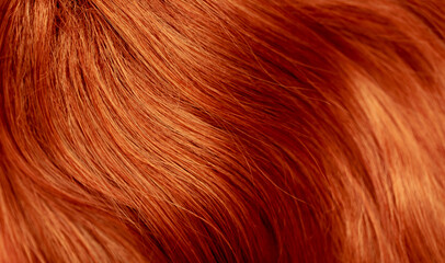 Red hair close-up as a background. Women's long orange hair. Beautifully styled wavy shiny curls. Hair coloring bright shades. Hairdressing procedures, extension.