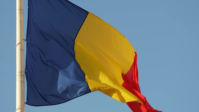 National flag of Romania. 4K video with Romanian flag waving against blue sky clear background in slow motion.