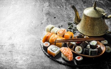 Rolls and maki on a stone stand with green tea in the teapot.