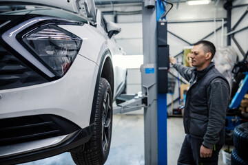 An auto mechanic is lifting car on a car lift at mechanic's shop.