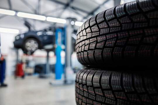 Selective focus on new tires at mechanic's shop with car in a blurry background.