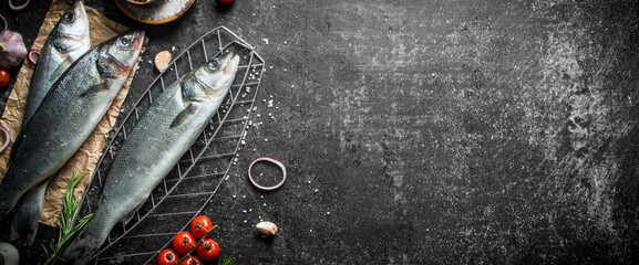 Raw fish seabass on a grid with tomatoes and spices.