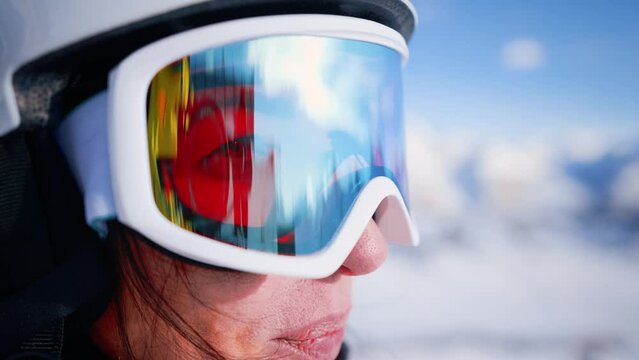 Close-up ski helmet and ski glasses with reflection mountains in snow on face young woman. Girl wear sport clothing in winter resort. Portrait beautiful female. Enjoy healthy rest, active lifestyle.