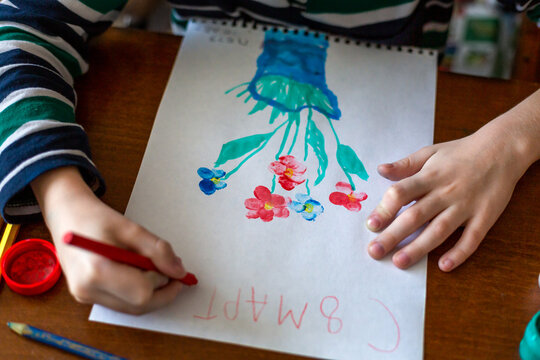 The hands of a child drawing flowers with gouache paints for mom by March 8