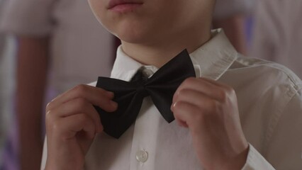 Close-up of a boy adjusting a bow tie. Action. cute boy touchingly adjusting bow tie on suit. 