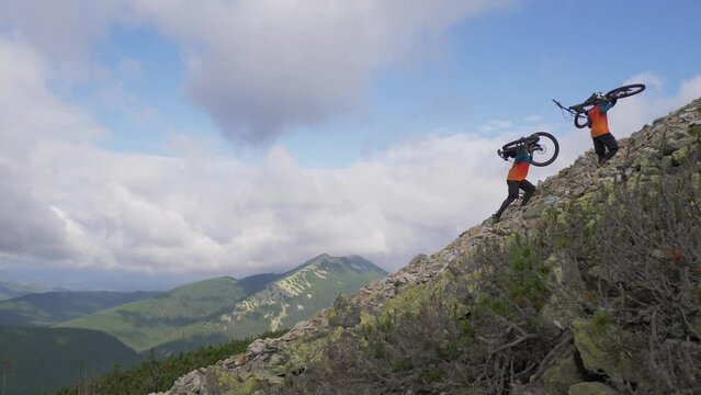 Two bikers go up the mountain with bicycles on their backs.
Rocky Mountain. 
Way with stones.
Freeride on bike.