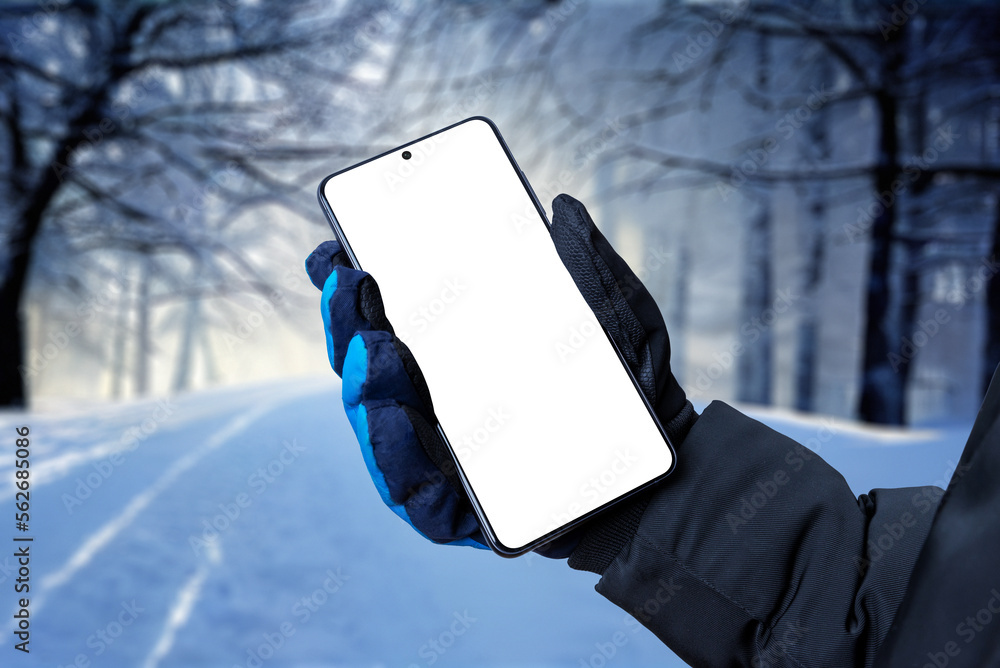 Poster mobile phone in hand with winter glove. trees covered with snow in background. isolated display for 