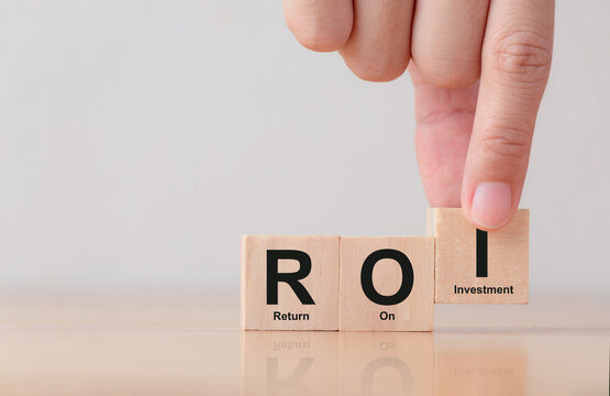 Hand puts wooden cubes with ROI on table. Medical and insurance concept