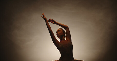 Beautiful caucasian ballet dancer performing, dancing and spinning on stage, spotted by searchlight and isolated on smoked black background close up 