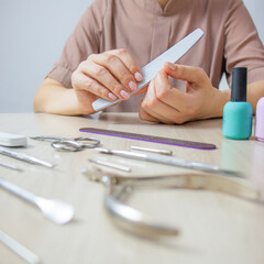 home manicure,  woman saws her nails with a nail file, manicure tools and nail polish lie on the...