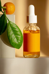 Orange serum with vitamin C in glass bottle with dropper lid and tangerine with green branch on...