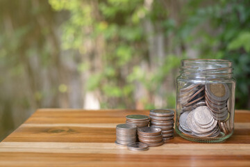 coin stacking on wood table and in side jar with natural background, concept of financial and money saving