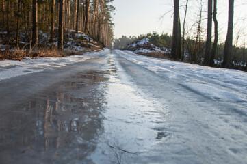 Icy forest road covered with a layer of water in winter. Dangerously.