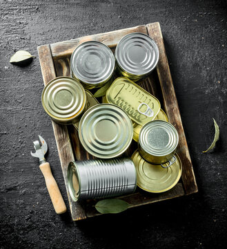 Closed cans of canned food on a wooden tray.