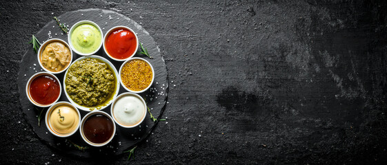 Pesto sauce, tomato sauce, barbecue sauce, mustard, mayonnaise, guacomole sauce on a stone Board.