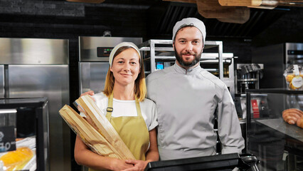 Portrait shot of Caucasian joyful couple of male and female bakers standing at bakehouse kitchen...