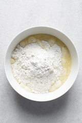 All purpose flour in a white bowl with milk and egg mixture