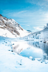 Fototapeta na wymiar Picturesque landscape of a snowy winter mountain lake. Small lake next to the Saut Deth Pish waterfall during autumn and a snowy day, located in the Aran Valley, Pyrenees, Catalonia, Spain.