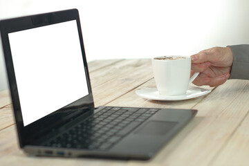 person in front of a laptop drinking coffee from a white cup