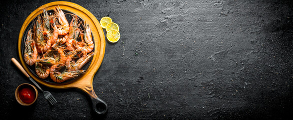 Grilled shrimps on a cutting Board with tomato sauce and sliced lemon.