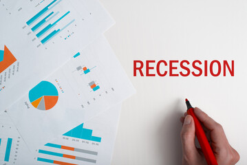 Economic downturn, financial crisis concept. Close-up hand writing word Recession with red marker, business documents with graphs and numbers on table, top view