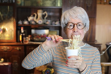 Senior woman eating instant noodles at home
