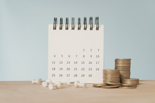 For payday loan concept. White calendar and blurred stack of coins , blurred white thumbtack on wood desk