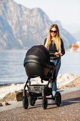Fototapeta na wymiar Young mother with stroller outdoor near the lake. Motherhood and healthy concept.