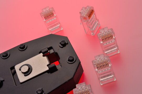 A rg45 connector for an internet cable and a twisted pair crimper lie on a multi-colored background. Close-up