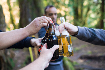 Men cheers their beer bottles in the forest.