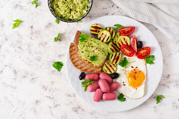 Fried egg with mini sausage, tomatoes, grilled zucchini, black olives and toasts with guacamole. English Breakfast. Brunch. Top view