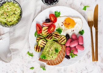 Fried egg with mini sausage, tomatoes, grilled zucchini, black olives and toasts with guacamole. English Breakfast. Brunch. Top view